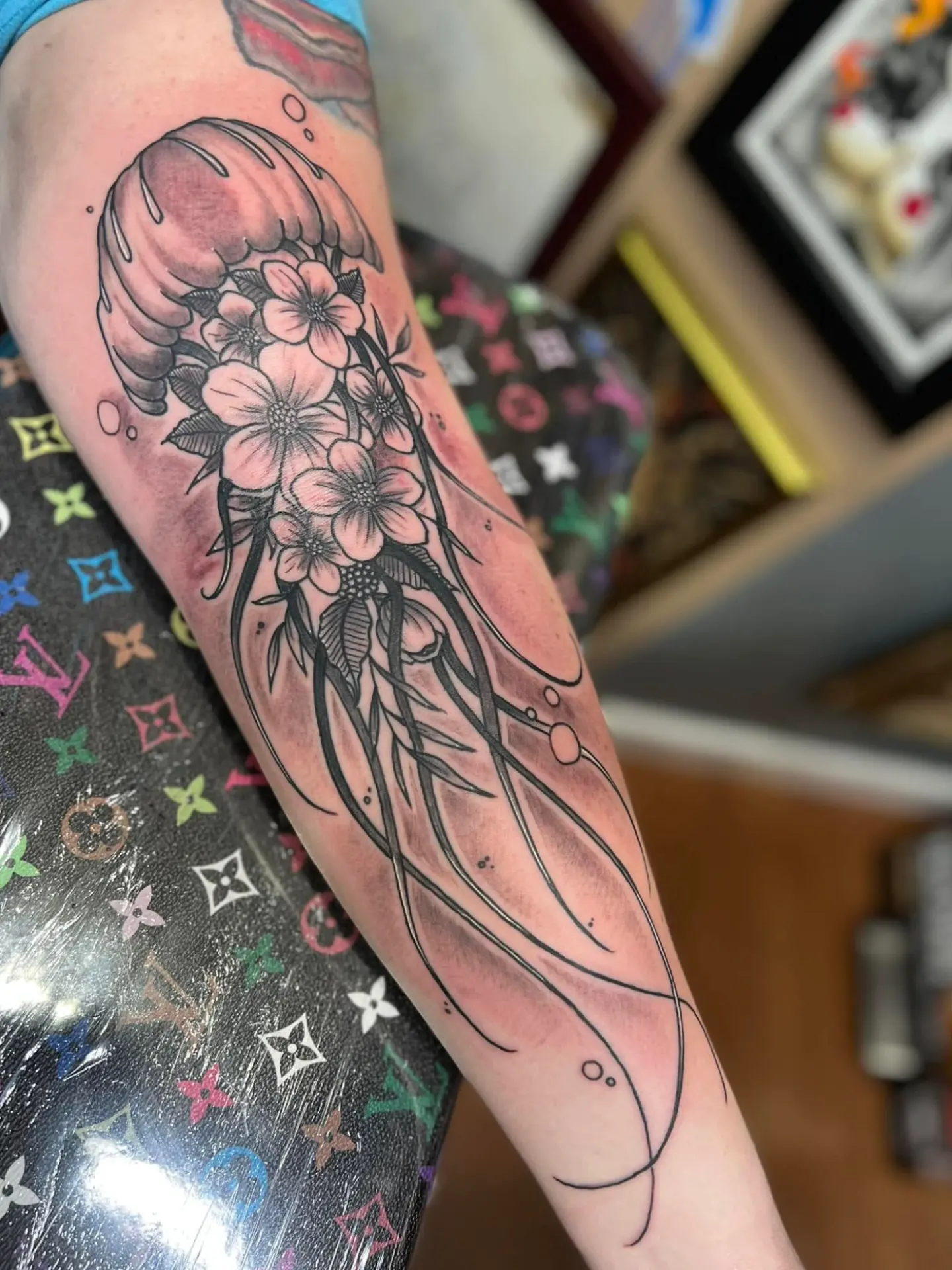 Fine line jellyfish and cherry blossom tattoo on a forearm