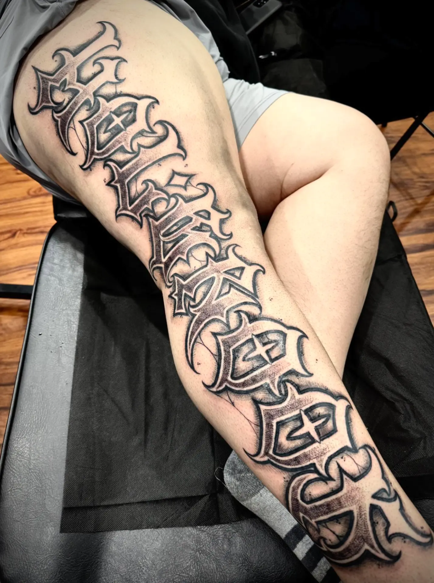 Large black and grey script lettering tattoo running down a leg